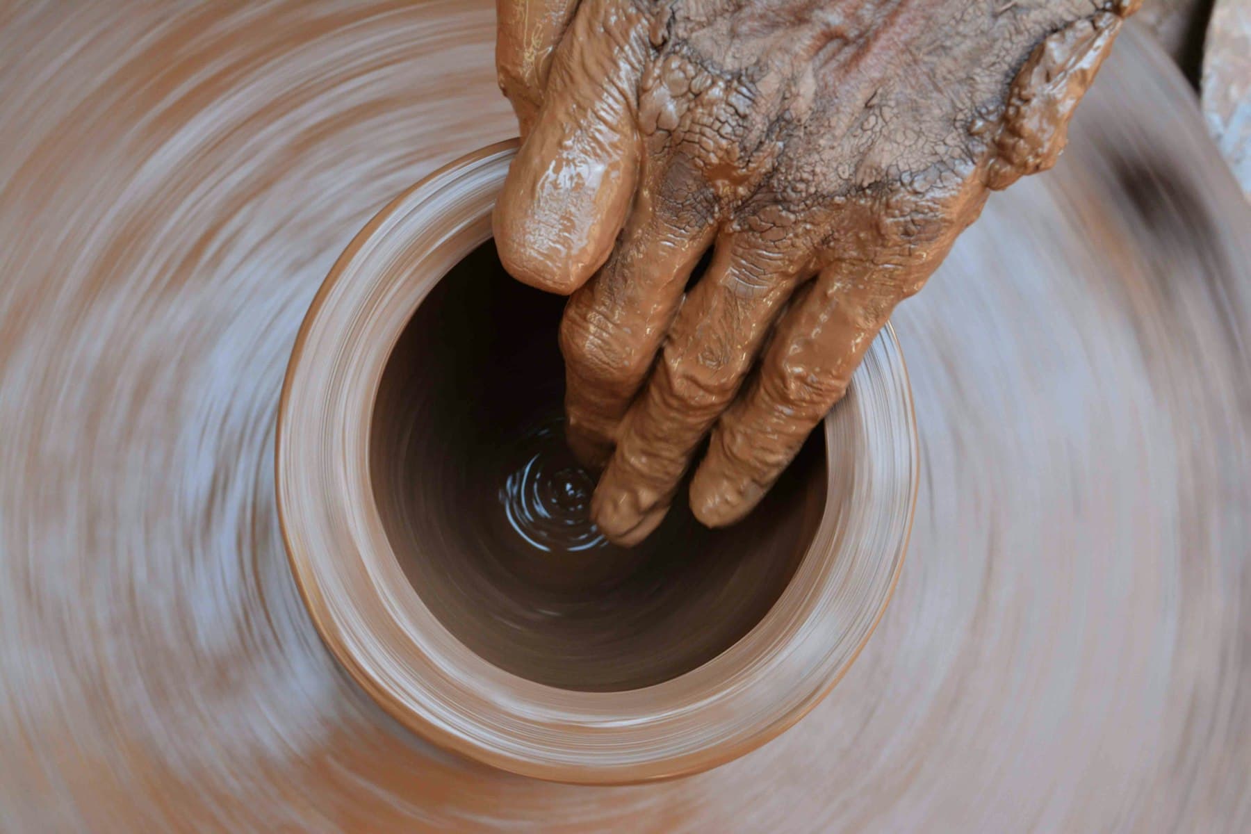 A potter’s hand shaping a clay pot on a spinning wheel